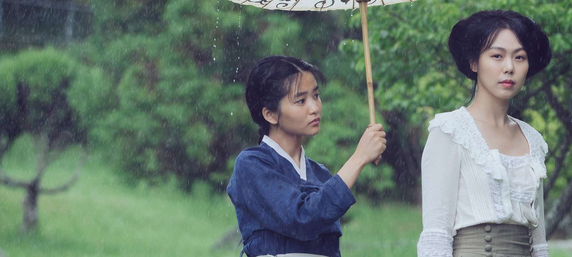 The Japanese heiress and her Handmaiden from the film The Handmaiden standing in a green area with the handmaiden holding an umbrella over the heiress.