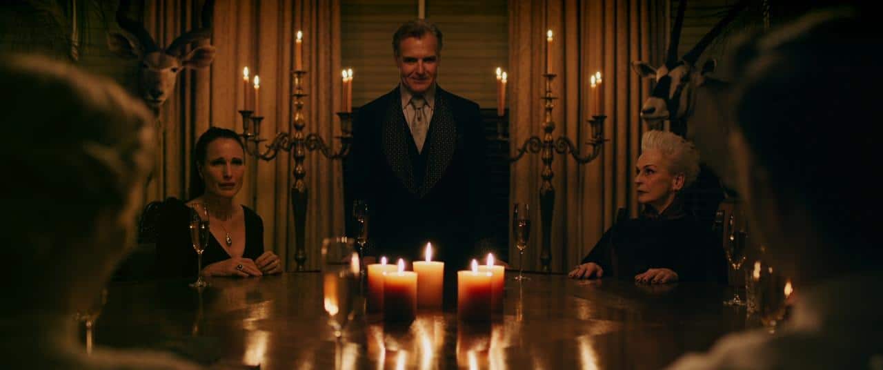 The characters of the movie sitting around a dining table in a candle lit room