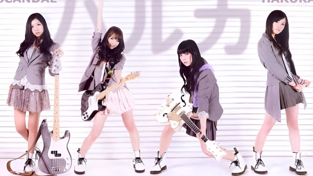 Four members of Japanese rock band SCANDAL posing together in a pink-themed setting.